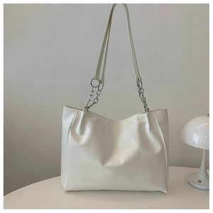 Detail of white PU leather tote bag with silver chain strap on a minimalist desk