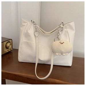 Detail of white tote bag with faux leather texture, chain strap, and plush charm on a desk
