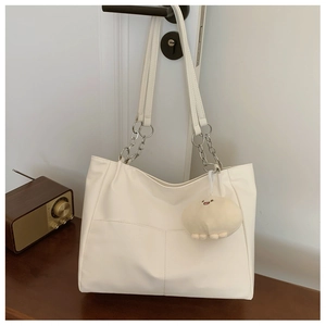 Close-up of white tote bag with silver chain handle and cute plush charm on a door