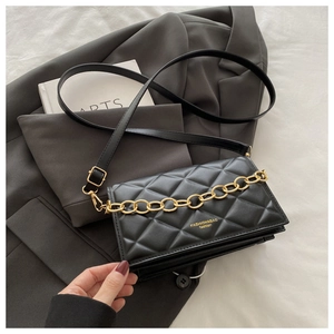 Close-up of black quilted leather bag with chunky gold chain on a grey blazer suit