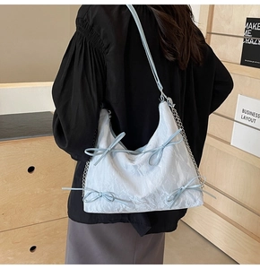 Détail d'un sac à bandoulière bleu clair plissé avec nœuds décoratifs et chaîne argentée