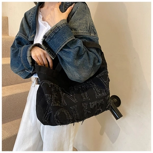 Dettaglio borsa tote in denim nero con bordi sfrangiati e toppe con lettere in 3D