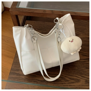 Detail of white PU tote bag featuring a front pocket and a cute smiley plush pendant