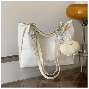 Detail of cream tote bag with silver chain handles and a white cloud plush charm