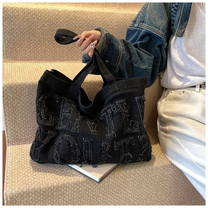 Dettaglio ricamo sfrangiato GENTLE YOUTH sulla borsa tote in denim nero con tracolla