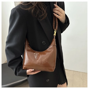 Detail view of brown patent leather hobo bag with embossed lettering and gold buckle