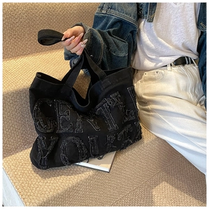 Dettaglio borsa tote in denim nero con ricamo GENTLE YOUTH e bordi sfrangiati