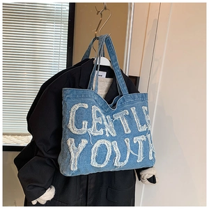 Dettaglio della borsa tote in denim blu con ricamo a toppa sfrangiata Gentle Youth bianca
