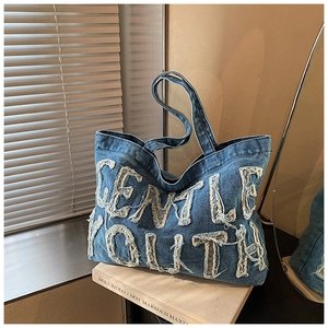 Dettaglio del ricamo Gentle Youth su borsa tote in denim blu con finiture sfrangiate