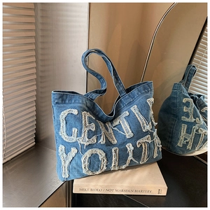 Dettaglio del ricamo GENTLE YOUTH e bordi sfrangiati sulla borsa tote in denim