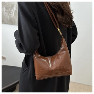 Brown patent leather hobo bag with embossed lettering worn by a model in a side view