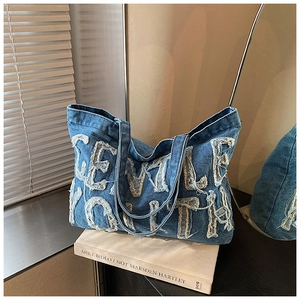 Dettaglio della borsa tote in denim vintage con ricamo di lettere bianche e spalline larghe