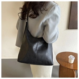 Close-up of a black pleated faux leather tote bag worn on a shoulder in a home setting