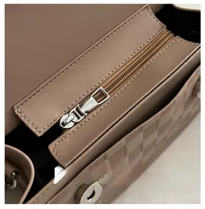 Detail of smooth silver metal zipper and checkered embossed leather on beige baguette bag