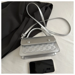 Detail of silver crossbody bag with checkered texture flap and metal buckle accents