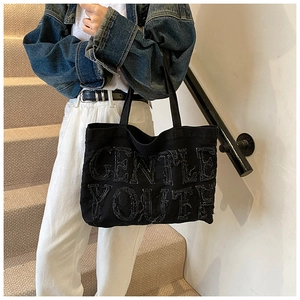 Dettaglio della borsa tote in denim nero con toppa Gentle Youth e bordi a taglio vivo