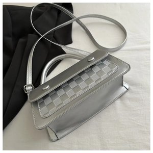 Detail of silver textured woven crossbody bag featuring cylindrical metal accents and strap