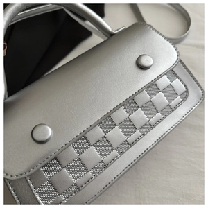 Detail of silver handbag featuring a modern textured grid pattern and round buckles