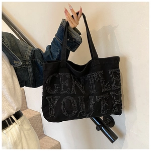 Dettaglio della borsa tote in denim nero con scritta Gentle Youth sfrangiata stile urban