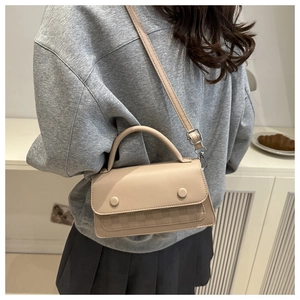 Side view of beige crossbody bag with quilted lattice texture on grey casual outfit