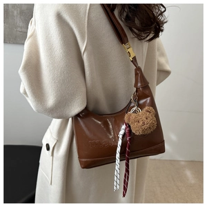 Detail of a brown crescent moon bag with debossed lettering and cute plush bear charm