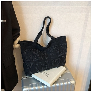 Dettaglio borsa tote in denim nero con scritta Gentle Youth su valigia argento