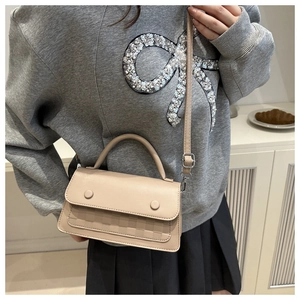Detail of beige crossbody bag featuring checkered embossed texture and button accents