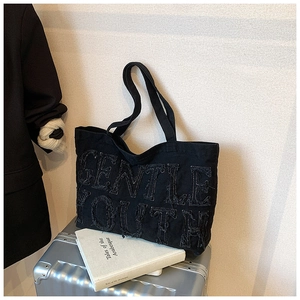 Dettaglio della borsa tote in denim nero con ricamo GENTLE YOUTH ed effetto sfrangiato