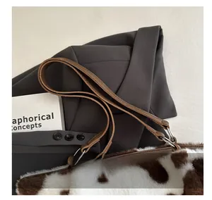Close-up of cow print plush tote bag with brown leather handles on a grey suit jacket