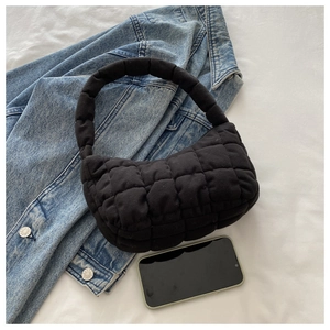 Close-up of black quilted puff handbag next to smartphone showing medium size and texture