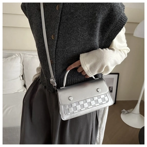 Silver metallic crossbody bag with woven texture and handle shown in a home setting