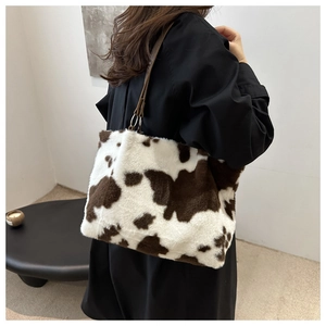 Detailed shoulder view of a soft cow-print plush tote bag with brown leather strap detail