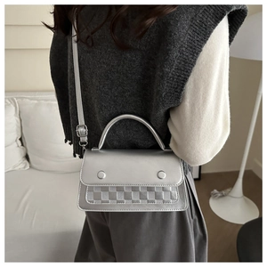 Detail of silver metallic handbag featuring a checkered texture strip and rigid handle