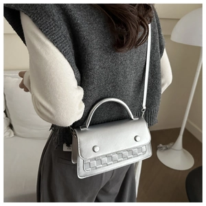 Detail of silver metallic crossbody bag featuring woven texture and round metal buckles