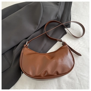 Detailed view of a dark brown crescent bag on a grey blazer and white tablecloth