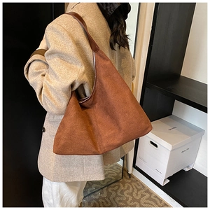 Side view of large brown suede hobo bag worn by a model in a minimalist setting