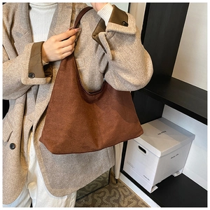Detail of brown hobo bag with wide strap worn with a plaid blazer and soft suede texture