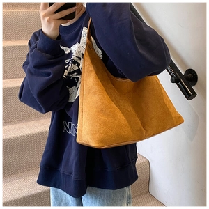 Side view of large brown suede tote bag worn on shoulder by a model on stairs