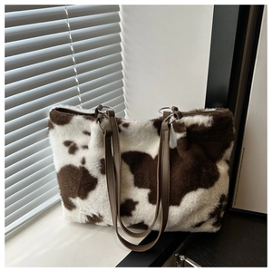 Close-up of cow print faux fur tote bag with brown leather straps and metal rings