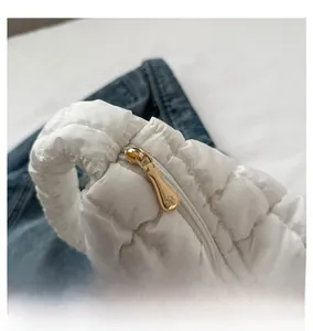 Detail of smooth gold metal zipper on white quilted cloud bag with romantic embroidery