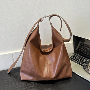 Brown vintage faux leather tote bag with silver buckle on a wooden desk with a laptop