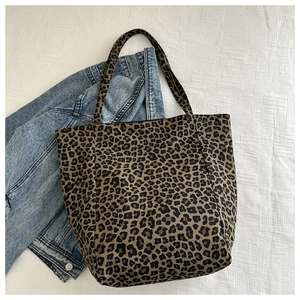 Détail du sac cabas imprimé léopard posé sur un tissu blanc près d'une veste en jean