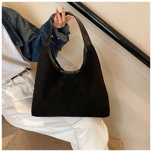 Detail of black suede tote bag with leather strap shown in a daily commuting scene