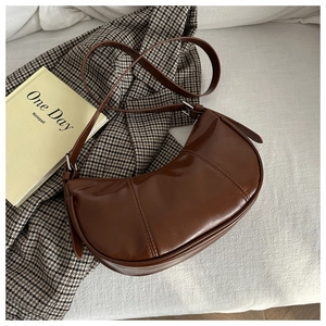 Detail of dark brown glossy leather underarm bag with decorative stitching and shoulder strap