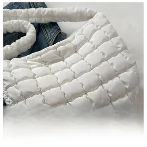Close-up of white quilted puffer shoulder bag showing soft padded texture on denim