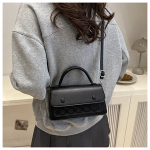 Detail of a black matte leather plaid crossbody bag showing weave texture and dual buckles