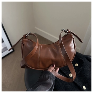 Detail of brown crescent leather bag showing glossy texture and silver metal buckle