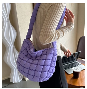 Close-up of a purple quilted puffer crossbody bag with a wide strap in a cozy cafe setting