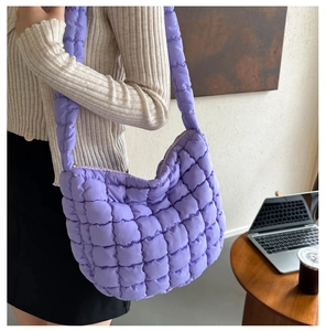Close-up of a purple quilted puff shoulder bag worn by a model in a modern office setting