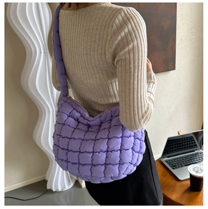 Lifestyle shot of a large lavender quilted cloud bag worn over the shoulder in a cafe setting